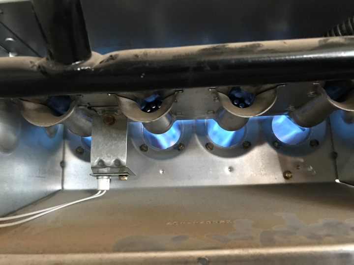 Close-up of gas furnace burners lit with blue flames