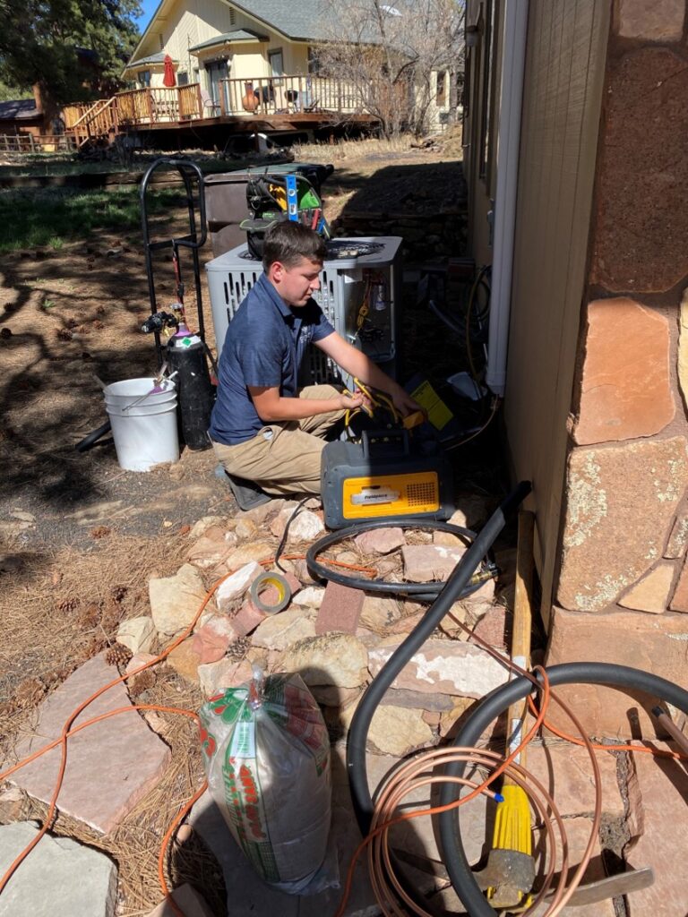 Legendary Energy technician servicing an outdoor unit with refrigerant recovery equipment