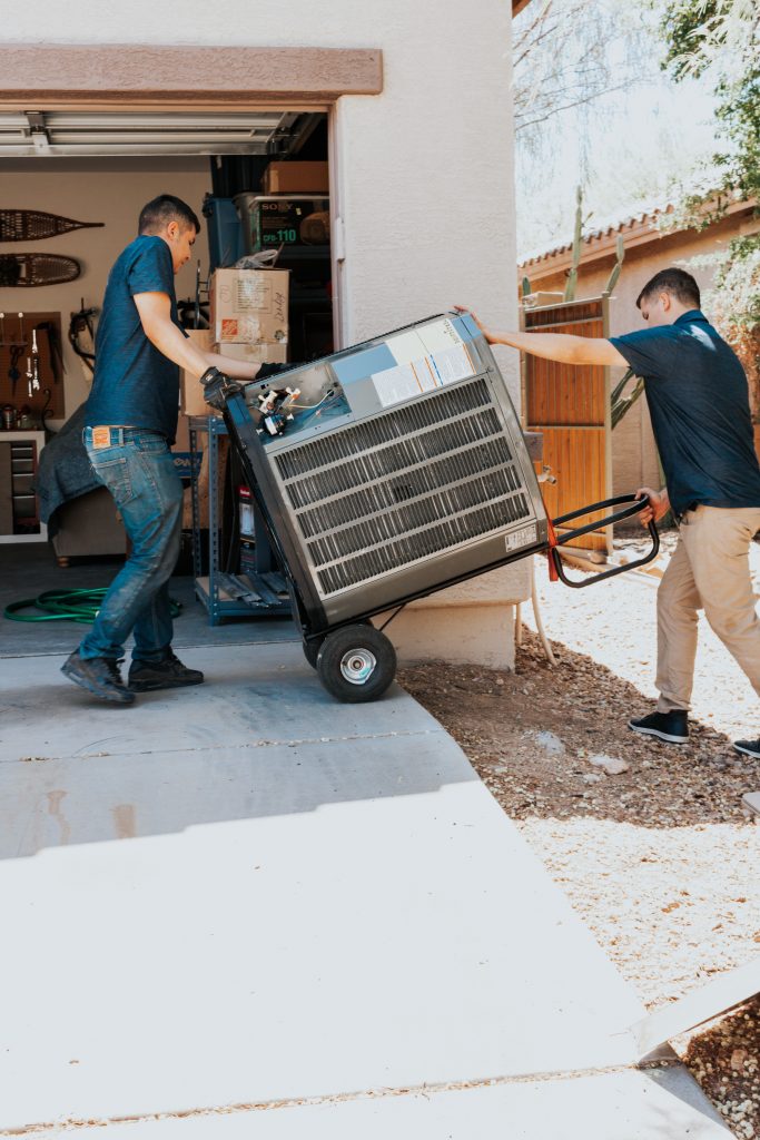 Two Legendary Energy technicians moving an old unit out on a hand truck