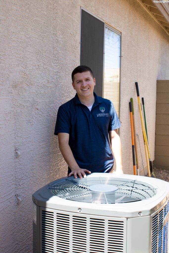 Legendary Energy technician smiling with his hand resting on a newly installed air conditioning unit