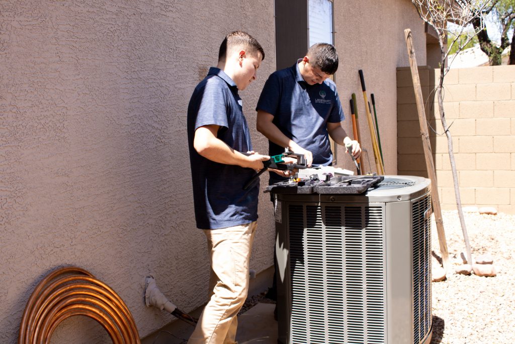 Two Legendary Energy technicians repairing an outdoor AC unit on an emergency service call
