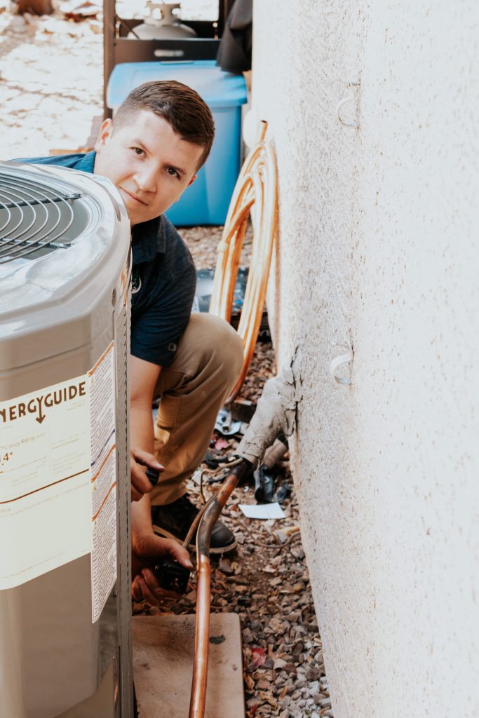 Smiling Legendary Energy technician beside an outdoor AC unit after getting it running again