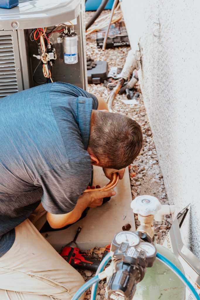 Legendary Energy technician checking the line connections at the base of an outdoor unit