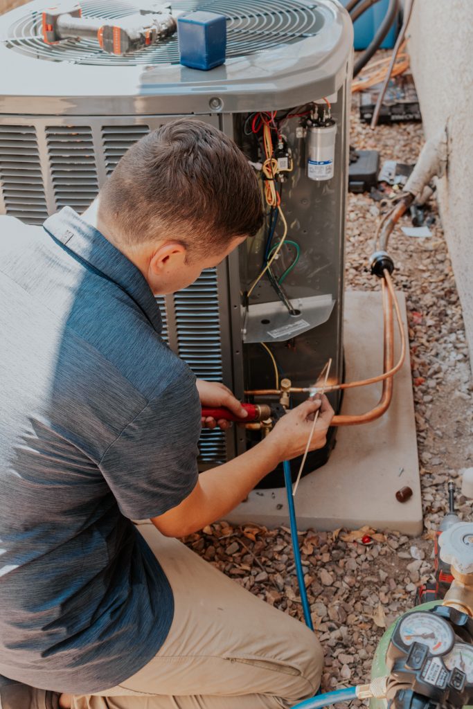HVAC technician brazing copper refrigerant lines with a torch while installing an air conditioning condenser unit