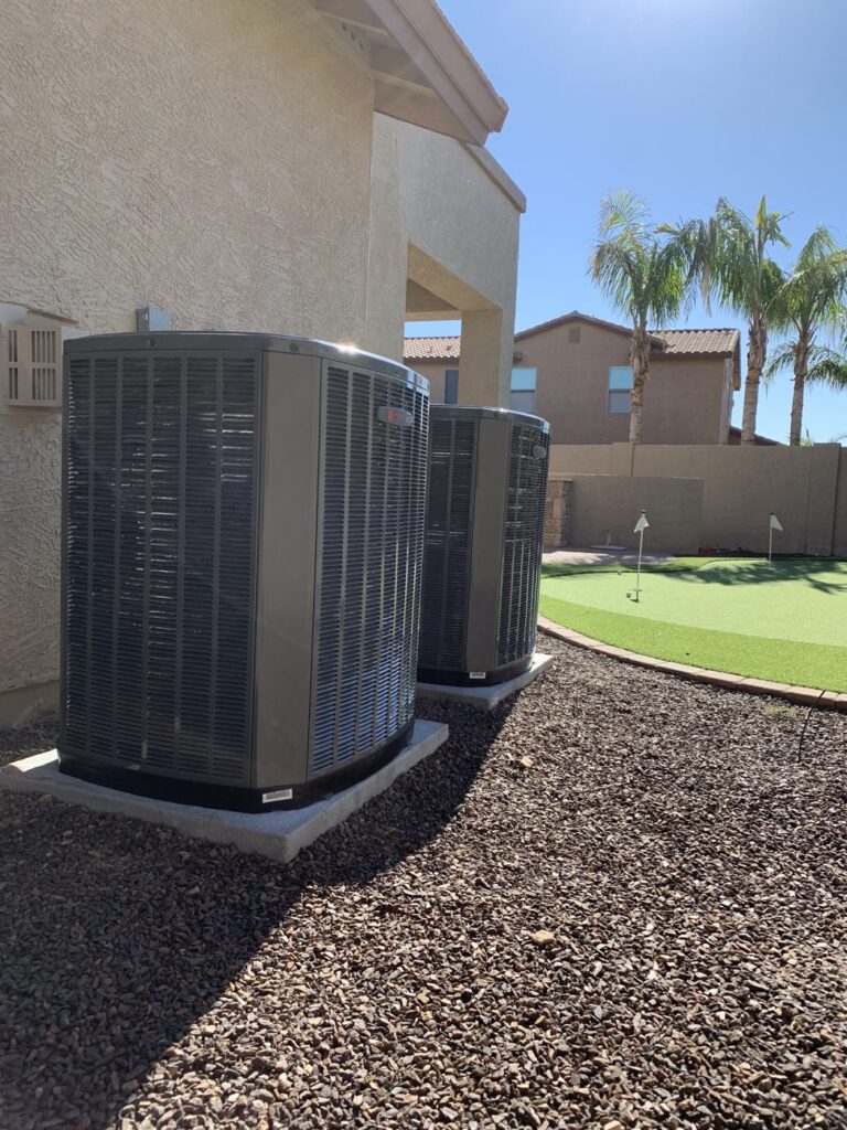 Two outdoor heat pump and air conditioning units on concrete pads beside a Phoenix home