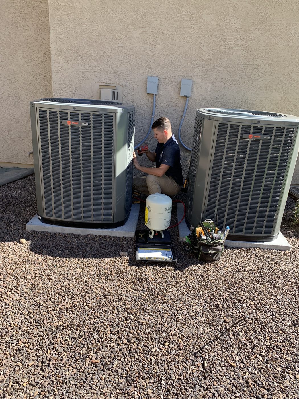 Legendary Energy technician servicing two outdoor units with a refrigerant tank beside him